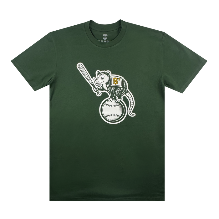 The Clutch Tee by Oakland Ballers showcases a cartoon opossum in a yellow "B" jersey with a bat, standing on a baseball, all on dark green fabric against a white background.