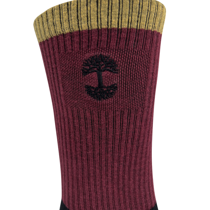 A close-up view of the Colorblock Sock by Oaklandish showcases its upper section, featuring a mustard-yellow band at the top, followed by a wider maroon section with vertical ribbing. An embroidered Oaklandish logo is knitted into the maroon section, and the lower part of the sock is black.