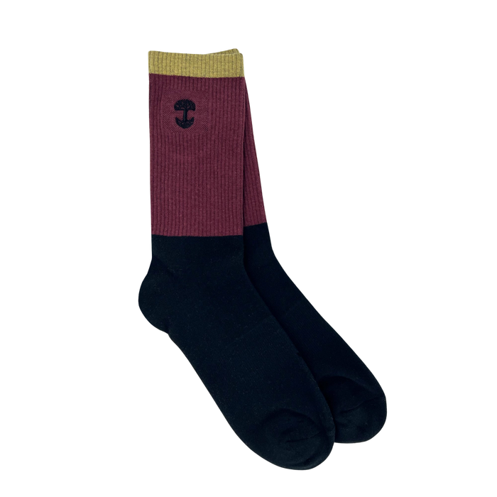 The Oaklandish Colorblock Sock features a unique color block design, with olive green at the top, a maroon middle section, and black covering the lower part. An embroidered Oaklandish logo adorns the maroon portion near the top. The background is plain white.