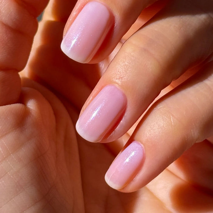 A close-up of a hand with short, naturally manicured nails painted in LONDONTOWN Conceal + Go Pink—a light pink, glossy polish that gives nails a fresh, understated look.