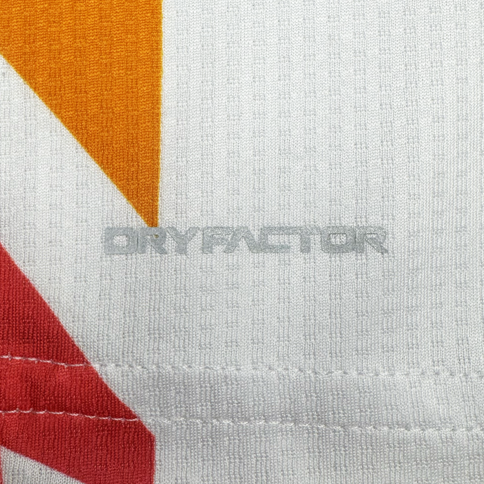 Close-up of a white textured fabric from the Custom Unisex Mosaic in Motion Kit by Oakland Roots SC, featuring orange and red geometric shapes. "DRYFACTOR" is printed in gray across the center, with visible stitching at the bottom edge.