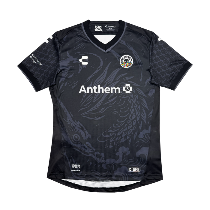 The Custom Unisex Oak-ness Awakens Kit by Oakland Roots SC is a black soccer jersey with a dragon graphic, round collar, Cuervos Negros and Charly logos on the chest, "Anthem" in white, and sponsor logos on both sleeves and above the hem.
