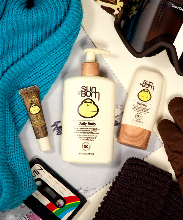 Sun Bum Daily + Lip Bundle with SPF 50 lotion and lip balm surrounded by winter accessories and a cassette tape