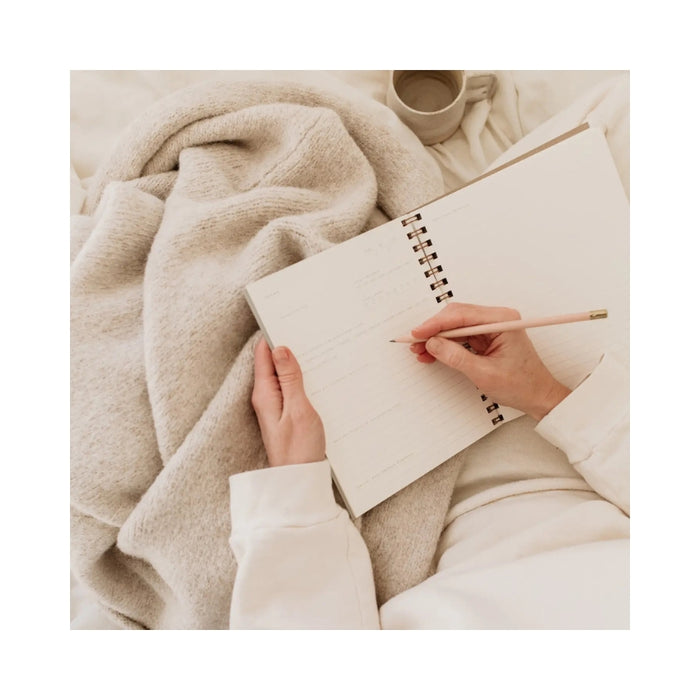 Person writing in a notebook with a pencil, surrounded by soft fabric