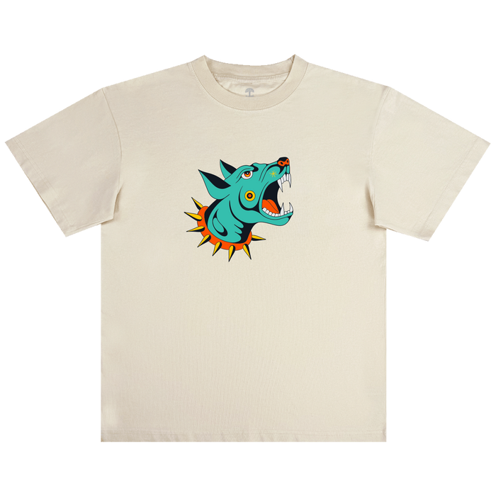 The Dawg Tee by Other is a beige, classic fit t-shirt made from 100% cotton, showcasing a bold, tattoo flash-inspired turquoise wolf head graphic at the center, with an open mouth revealing sharp teeth, vivid orange and yellow spikes around its neck, and an intense expression.