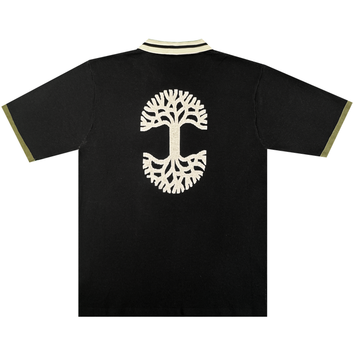 The Oaklandish Ease Jersey is a black unisex polo with beige knit collar and trim, featuring a large embroidered beige tree on the back with mirrored branches and roots in a circular design.
