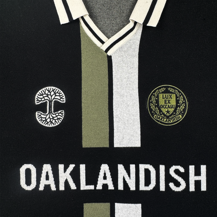 The Oaklandish Ease Jersey is a unisex black knit-collar top with white and olive-green stripes, two embroidered patches, and bold "OAKLANDISH" lettering across the chest.