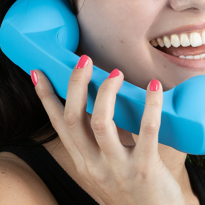 A person smiles, holding a blue retro-style phone handset with LONDONTOWN's Electric Flamingo nails flaunting vibrant pink polish.