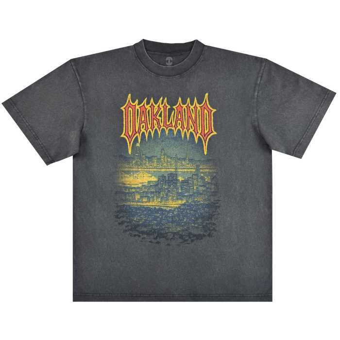The Oaklandish Ember Tee is a faded black classic fit, 100% cotton shirt featuring "OAKLAND" in bold yellow and red above a detailed blue Oakland skyline graphic on a glowing background for a cool nighttime vibe.