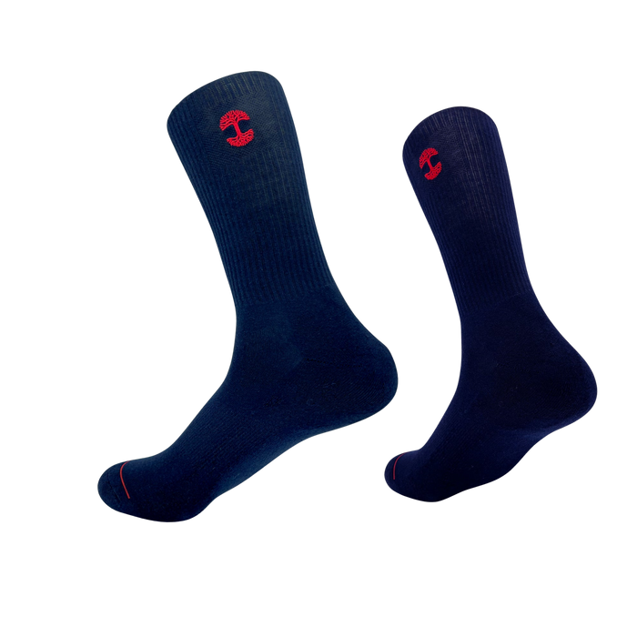 An image of the Embroidered Logo Sock by Oaklandish features two dark blue crew socks, each adorned with a red embroidered Oaklandish logo near the top. The socks are positioned upright with toes slightly pointed downward, creating a floating appearance against a white background. The adult-sized socks also have ribbed cuffs and a red accent line near the toes.