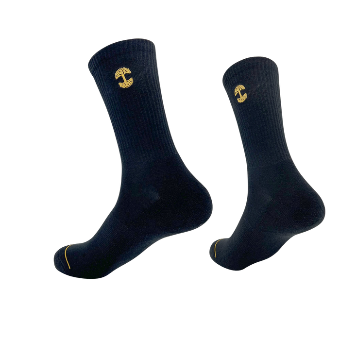 Two Embroidered Logo Socks from Oaklandish, made in a ribbed material with a black and gold color scheme, are shown against a plain white background. These crew socks showcase the iconic yellow Oaklandish logo near the top and a subtle yellow detail near the toe area. They appear to be mid-calf length and are slightly elevated, giving the impression of floating.