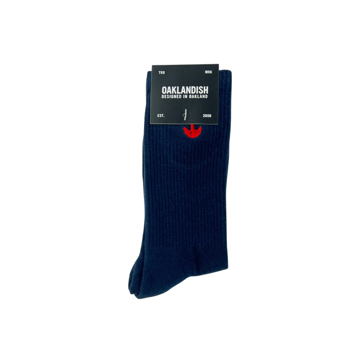 A pair of dark blue Embroidered Logo Socks is neatly folded, secured with a black label that reads, "OAKLANDISH, Designed in Oakland" with "EST. 2000" below. The adult-sized socks feature a subtle red embroidered Oaklandish logo near the top and have a ribbed texture.