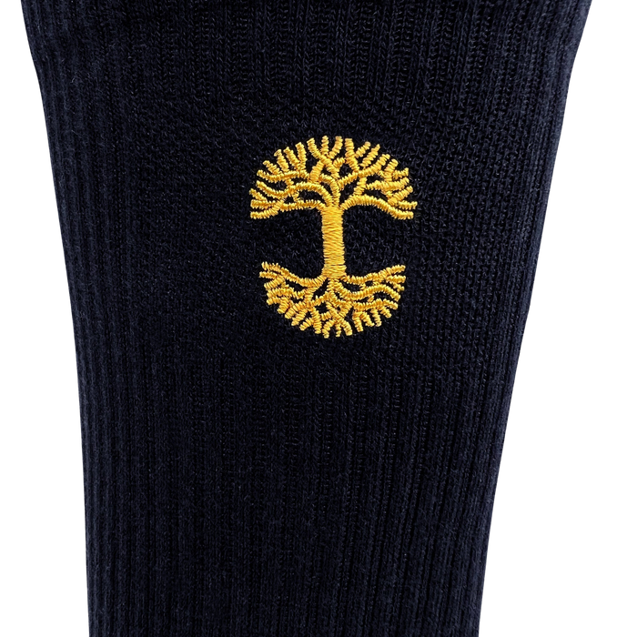 A close-up of the Embroidered Logo Sock by Oaklandish, featuring black and gold ribbed fabric and an intricate yellow tree with detailed roots and branches. The symmetrical design is centrally placed, creating a striking contrast against the dark background.