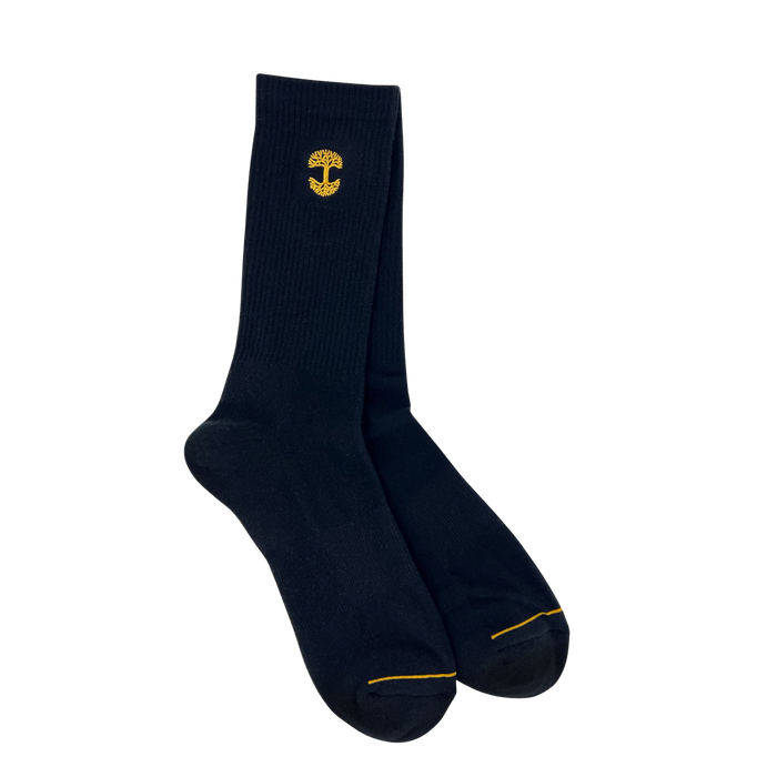 The Embroidered Logo Sock by Oaklandish is a pair of black/gold crew socks, featuring a small yellow mushroom logo embroidered near the top. These adult-sized socks have a ribbed texture on the upper portion and smooth fabric on the foot area, as well as reinforced toes stitched with yellow thread for added durability.