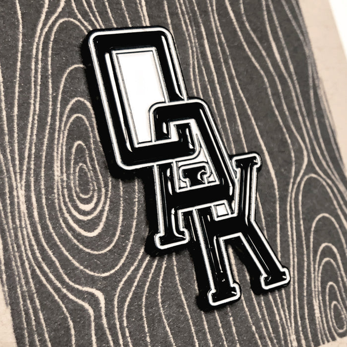Close up of  black OAK wordmark with white trim on enamel lapel pin.