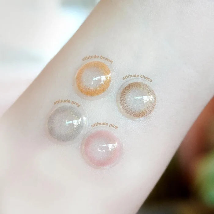 A close-up of a light-skinned arm displays four EyeCandys Attitude Glitter Set colored contacts, each showcasing a unique natural shade—perfect for party looks.