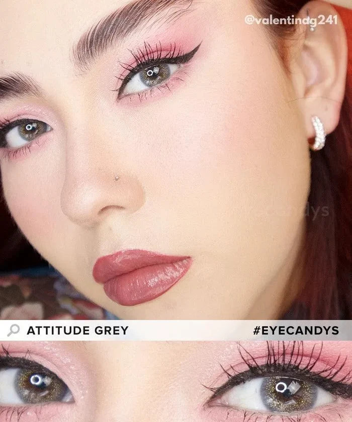 A close-up of a person with pink eye makeup, winged eyeliner, and EyeCandys Attitude Glitter Set (For Party Looks) colored contacts. They have light skin, glossy pink lips, and a nose stud, with "ATTITUDE GREY" and "#EYECANDYS" displayed.