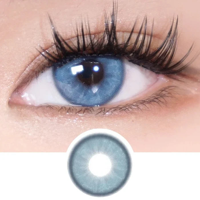 A close-up of a human eye with long lashes, wearing EyeCandys Doe Blue colored contacts with a natural iris design. Below is an enlarged image of the lens from EyeCandys, showcasing its detailed pattern.