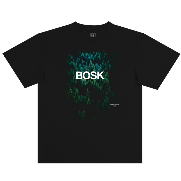Introducing the Forest Brush Tee by Other—a classic fit black t-shirt featuring an image of dense green forest trees. Bold white “BOSK” lettering is printed across the forest graphic, honoring the spirit of BOSK OUTDOORS, while subtle white text accents the lower right corner. Crafted from heavyweight cotton for comfort and durability, this tee stands out beautifully against a plain white background.