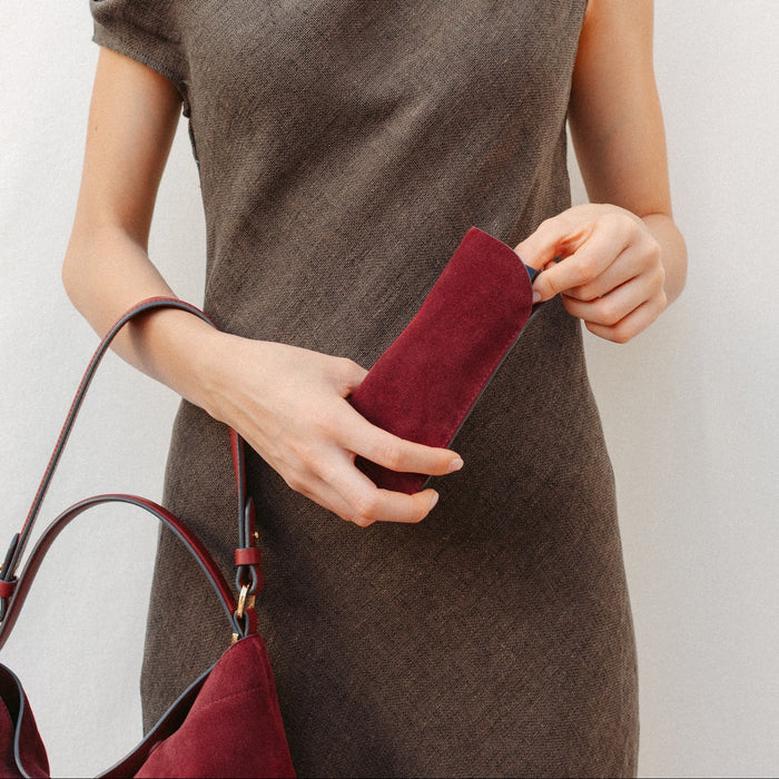 Model putting her glasses into STOW London's Glasses Case in Burgundy suede leather with the Burgundy suede Curve on her arm