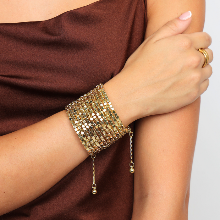 BuDhaGirl Gold Omega wrist wrap with cube cut metallic beads styled as a wide layered cuff with dangling ends on a womans wrist