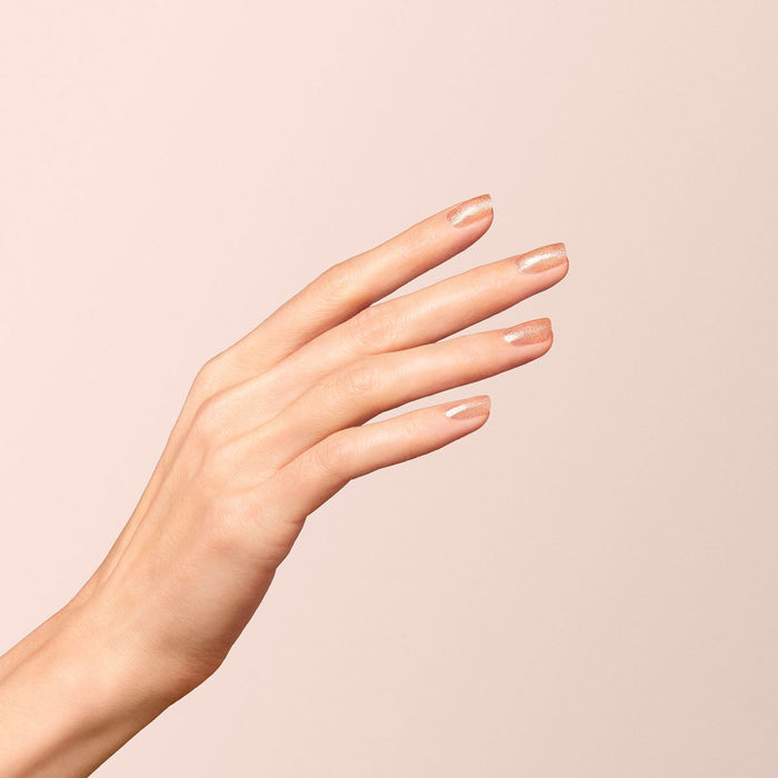 A hand with light skin tone and short, natural nails painted with Manucurist Green Flash gel polish in the shade Gold, against a soft beige background.