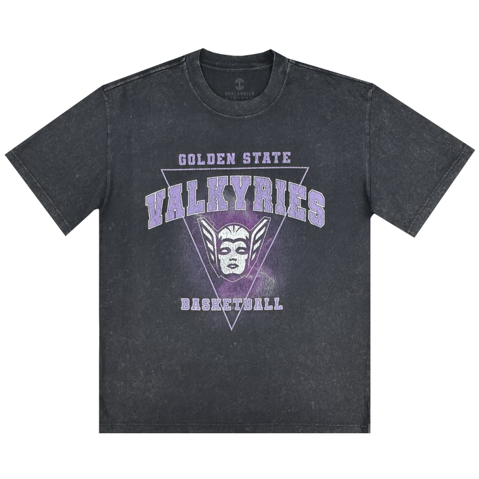 The GSV Golden State Valkyries Surge Stone Wash Heavy Tee is a black acid-wash shirt with "Golden State Valkyries Basketball" in white and purple, a stylized Valkyrie mask and purple triangle on the front. Made from soft organic cotton, with short sleeves and a relaxed fit.
