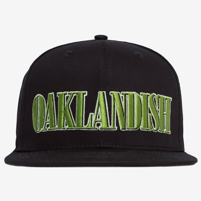 The Greenback Snapback by Oaklandish is a black cap with the word "OAKLANDISH" embroidered in large, green, capital letters on the front. This headwear features a flat brim and six ventilation eyelets, with two visible in this view.