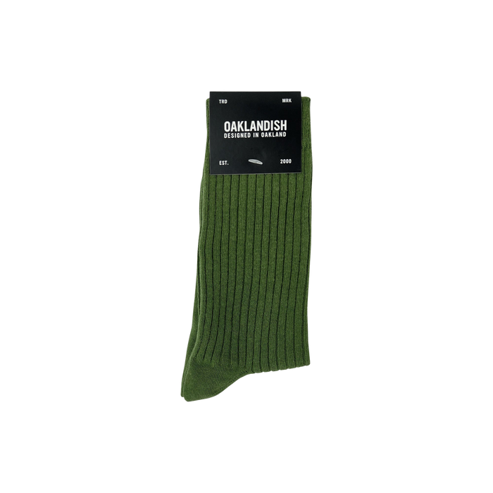 The Grip Crew Socks are shown in green with a ribbed texture. Packaged with a black label stating "OAKLANDISH Designed in Oakland" along with other text, these one-size-fits-most socks are neatly folded. The label is placed at the top against a plain white background.