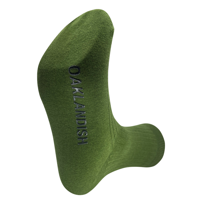 A Grip Crew Sock from Oaklandish in green, featuring the word "OAKLANDISH" woven in black thread running vertically along the side. This "one size fits most" sock is displayed clearly against a light gray background to showcase the text.