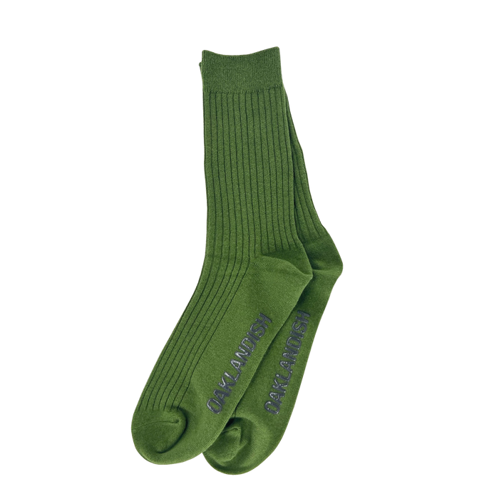 A pair of green Grip Crew Socks by Oaklandish, featuring "BANKAI INVANZO" vertically printed in blue along the outer sides. These one-size-fits-most socks are neatly laid out flat on a plain white background, showcasing their stylish design.