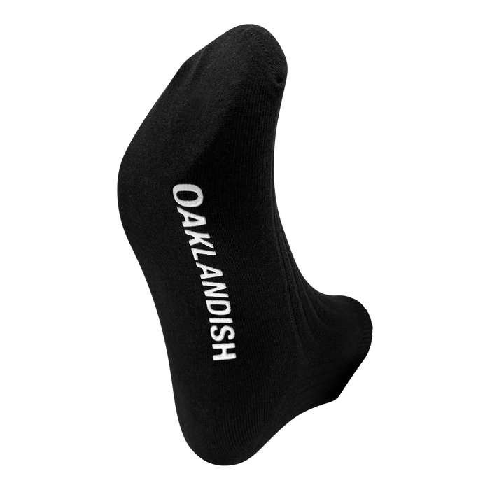 A single Grip Low Crew Sock by Oaklandish is displayed with the foot area facing forward. The sock features the word "OAKLANDISH" written in white capital letters along its sole. The plain white background perfectly highlights the Oaklandish sock.