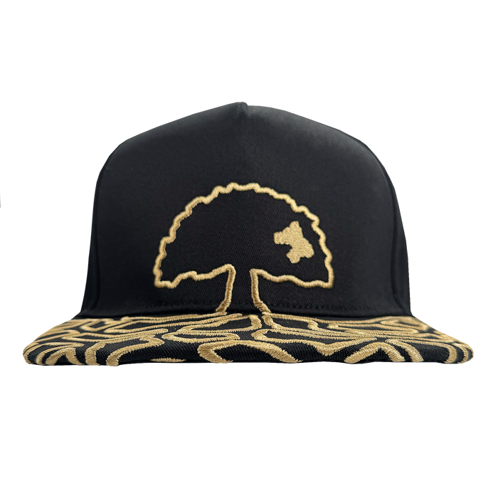 The Growth Cap by Oakland Roots SC is a black 5-panel snapback hat with a stylized gold tree embroidered on the front and abstract gold patterns on the flat brim, shown on a transparent background.