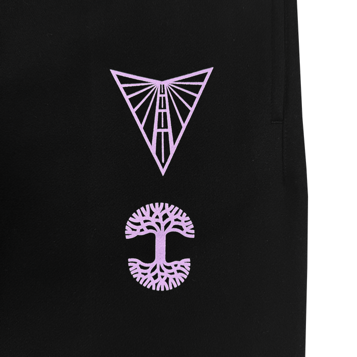 The GSV Renowned Pant by GSV is a black fleece sweatpant with two pink, vertically centered designs: an abstract triangular geometric symbol above and a stylized tree with spreading branches and roots forming a circle below.