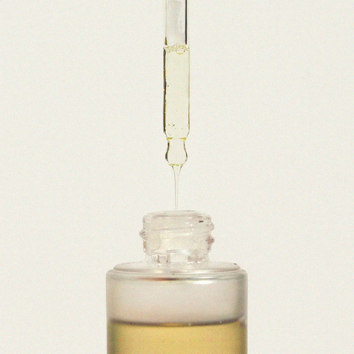 Glass dropper bottle with liquid being dispensed on a light beige background