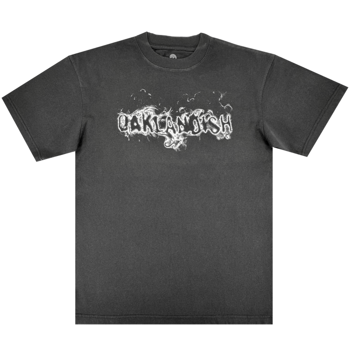 The Oaklandish Haze Tee is a men's black heavy-weight cotton t-shirt with a white, graffiti-style "OAKLANDISH" design in smoky letters on the chest. Classic fit with short sleeves and a crew neckline.