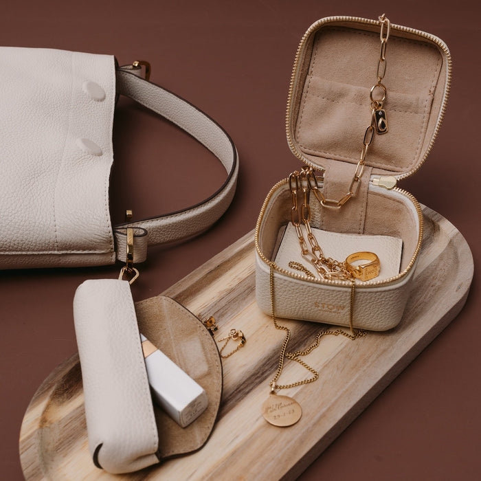 STOW London's Hester Jewellery Case in Spring Moon pebbled leather filled with gold jewellery, alongside the Spring Moon Lipstick case and Midi Curve on a wooden platter.