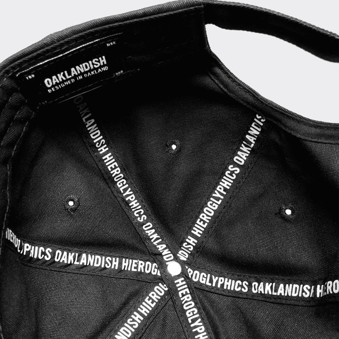 The image depicts the interior of a Hiero Logo Dad Hat by Hieroglyphics. The inner band features white text that repeats "OAKLANDISH HIERGLYPHICS." A label at the back reads "OAKLANDISH" and "DESIGNED IN OAKLAND" in white. The inner seams fan out from the central button.