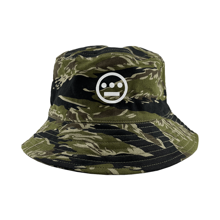 Introducing the Hieroglyphics Hiero Reversible Camo Bucket: A stylish bucket hat featuring a green and black tiger camo pattern, adorned with a white embroidered hieroglyphic symbol on the front. The unique symbol showcases a horizontal line with three dots above it, encased within a circle. This versatile hat boasts a wide, stitched brim and offers a relaxed, casual fit perfect for any occasion.