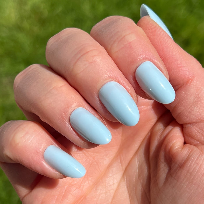 Close-up of a hand wearing Honest & True | Almond | Medium serene blue medium almond shaped press-on nails in natural sunlight