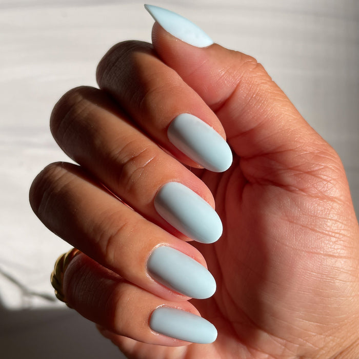 Hand displaying Honest & True | Almond | Medium serene blue almond-shaped press-on nails in natural light for at-home mani
