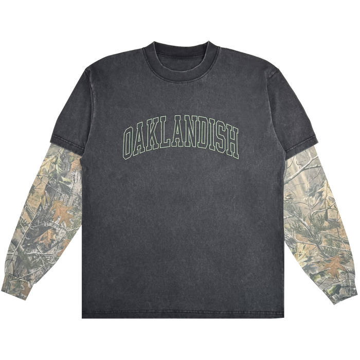 The Oaklandish Hunter LS Tee is a black washed crewneck with bold, arched green "OAKLANDISH" text and camo sleeves under short sleeves. Made from 100% cotton, this standout shirt is shown against a white background.