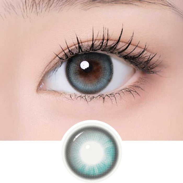 A close-up of an eye with long lashes wearing i-Girl One Pick Becca Matcha Blue contacts in a blue-gray shade. An enlarged image of the i-Girl lens is shown below the eye for detail.