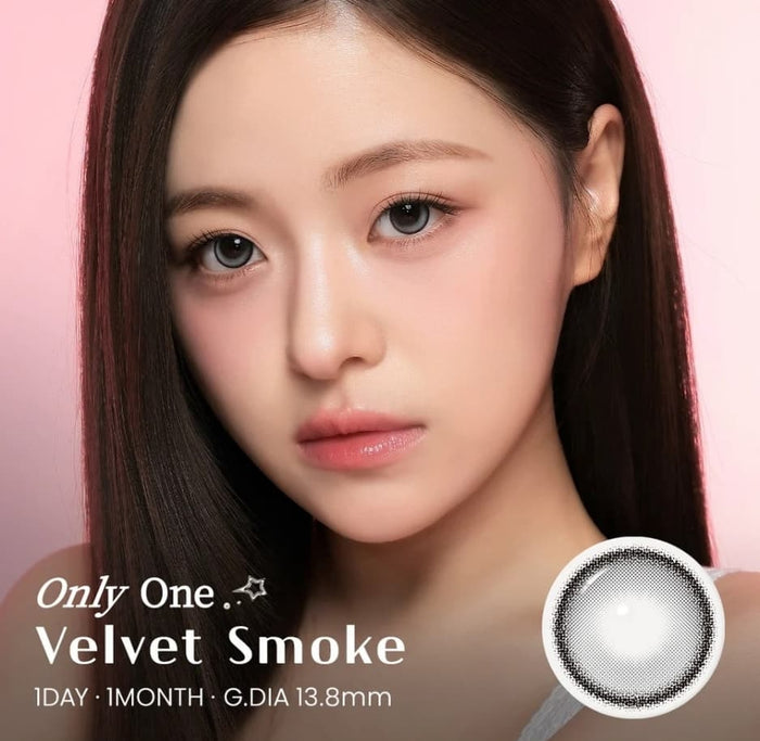 A young woman with straight black hair poses before a pink backdrop, wearing subtle makeup and i-Sha One Pick Only One 1-Day Velvet Smoke Grey (10pk) contacts. A close-up reveals the 3-tone gradient lens and “G.DIA 13.8mm.”.