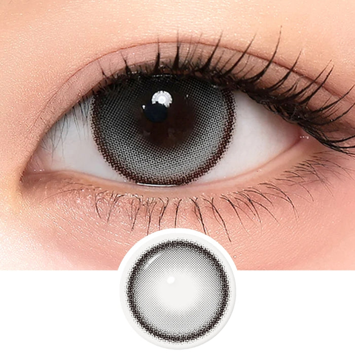 A close-up of a human eye wearing i-Sha One Pick Only One Velvet Smoke Grey contacts from i-Sha, featuring a dark, patterned lens that enhances the eye’s allure. An image of the lens design is shown below the eye, highlighting how natural-looking colored contacts like these Velvet Smoke Grey lenses can beautifully transform your gaze.