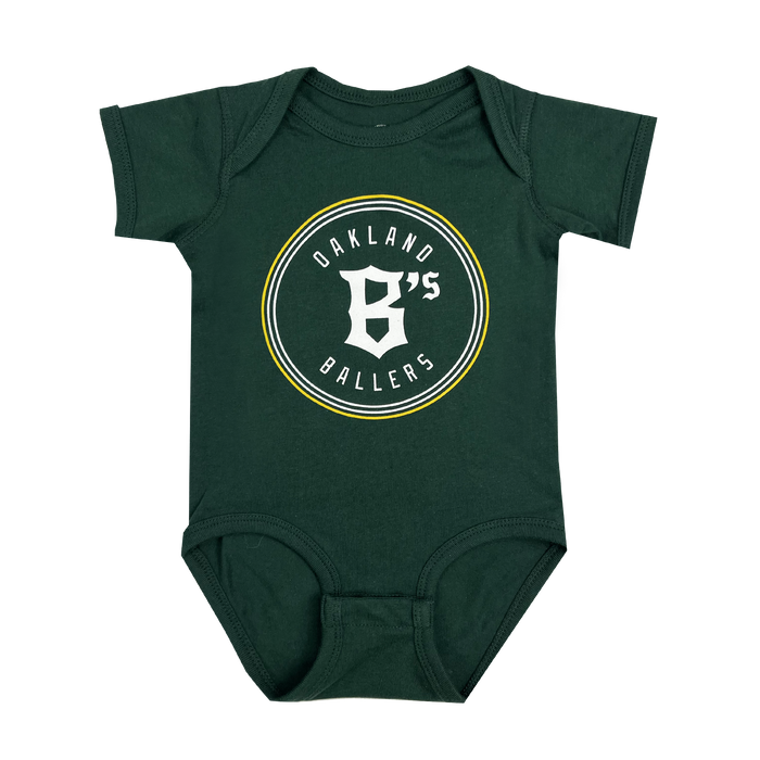 The Infant Oakland Ballers Logo One-Piece is a small, green baby onesie with short sleeves. The front showcases the "OAKLAND B'S BALLERS" logo, emphasizing their West Coast franchise. The logo features thin yellow, gray, and white concentric circles. For convenience, the onesie includes two snaps on each shoulder and three snaps at the bottom for easy dressing.