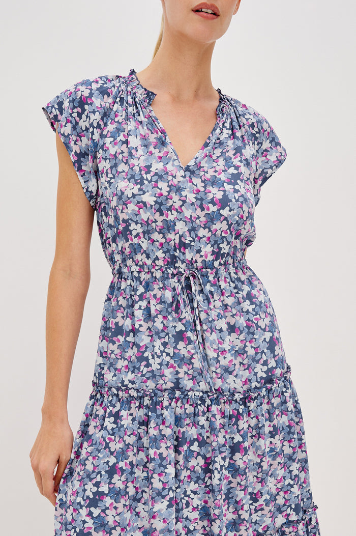 Juni Tiered Midi Dress with a V-Neck, Ruffled Neckline, Short Flutter Sleeves, Drawstring Waist Detail in Blue Blossom Colorway. Front View Shown on Model.