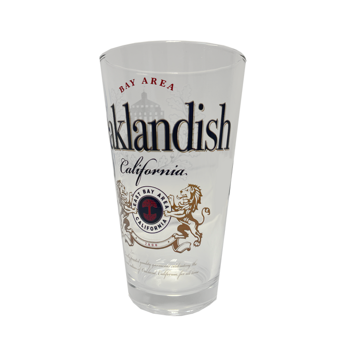 The **Lager Pint Glass** by **Oaklandish** is a stylish 16 oz pint glass featuring "Oaklandish" and "California" in bold black text. Above "Oaklandish," "Bay Area" is written in red, while below, a circular emblem displays "Bay Area California" flanked by two lions. The background of this practical drinkware is white, combining local pride with everyday functionality.