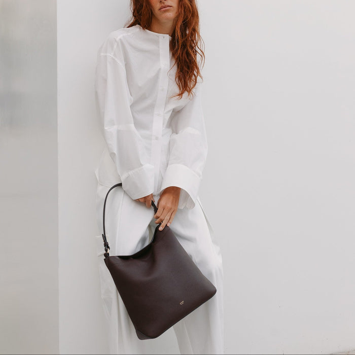 Model wearing STOW London's Curve Bag in Espresso pebbled leather featuring the detachable shoulder strap and gold-coated stainless steel hardware