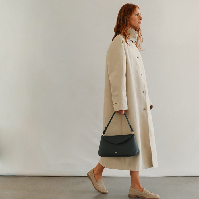 Model holding STOW London's East West in New Forest pebbled leather featuring the detachable shoulder strap and gold-coated stainless steel